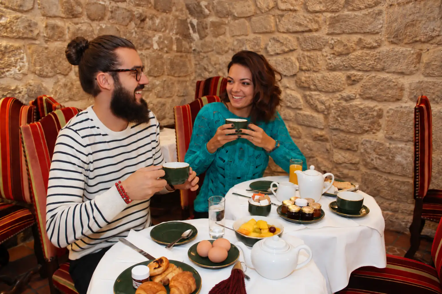 Couple prenant le petit déjeuner dans la cave voûtée en pierre, viennoiseries et fruits frais